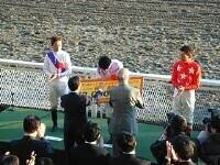 優勝した見澤騎手に、佐々木竹見さんと表彰式に飛び入りで参加していただいた原良馬さんから賞金２００万円の記念プレートが送られる。左は第２位・岩田騎手、右は第３位・的場騎手